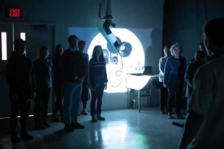 Group of students stand in darkened classroom with spotlit area