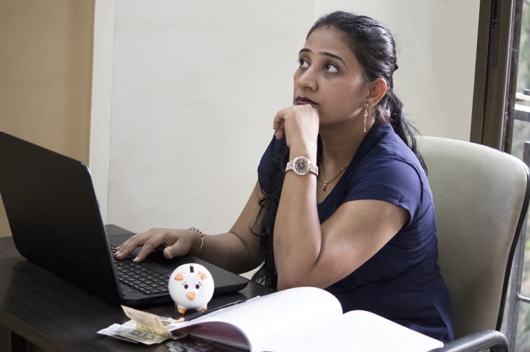 Woman of color sitting at a computer with a piggy bank