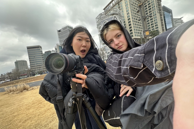 Two women behind a camera on tripod in urban landscape