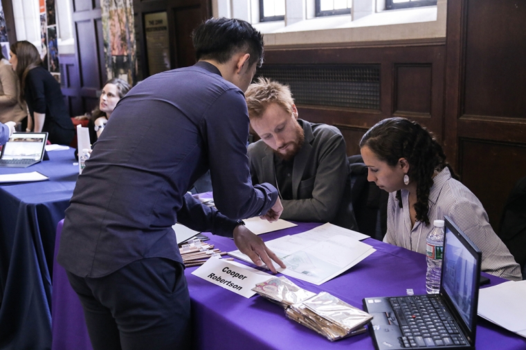 A student stands over a table showing his work to employers