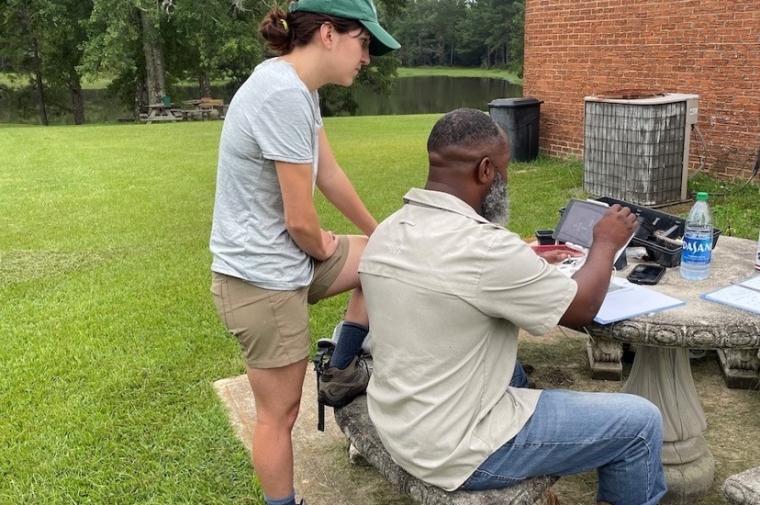 Two people work on computer monitor outside