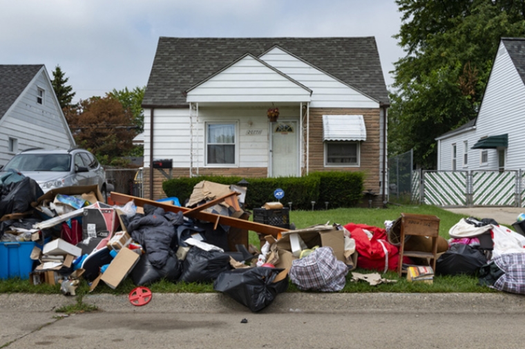Piles of trash and furniture left on the curb in front of a small house