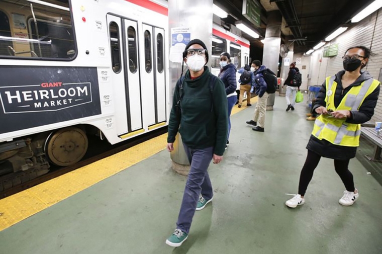A masked man wearing glasses is walking through a trolley station