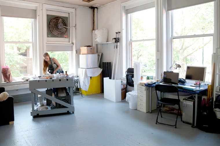 In a large studio space with large windows a student works at a work table in the middle of the room