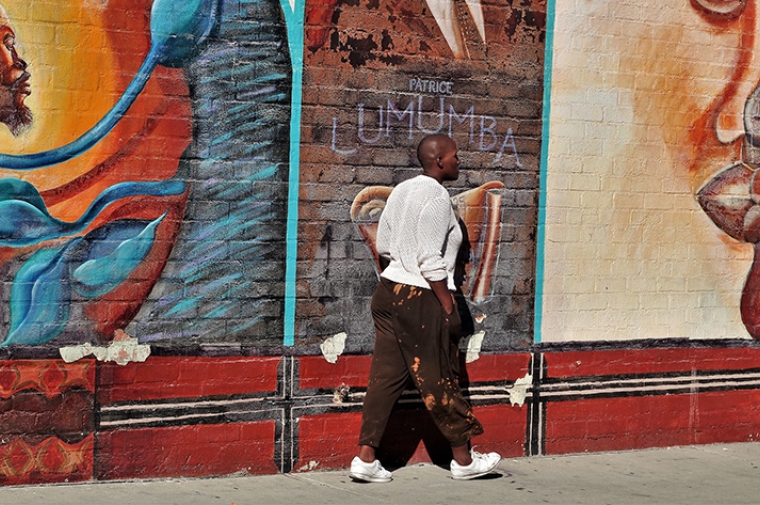 A person walking down the sidewalk next to a wall painted with a mural