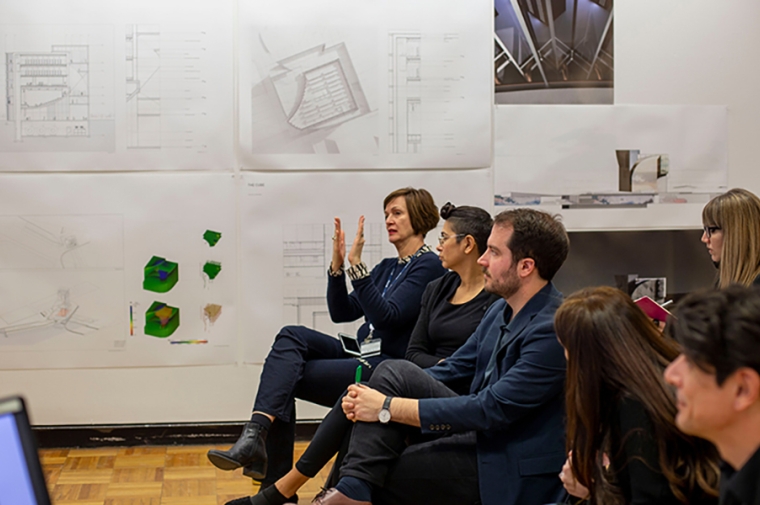 Seated reviewers looking to the side with renderings pinned to the wall behind them