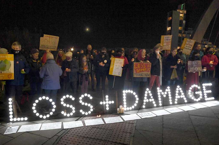 Crowd gathers behind a sign made of lights spelling Loss + Damage