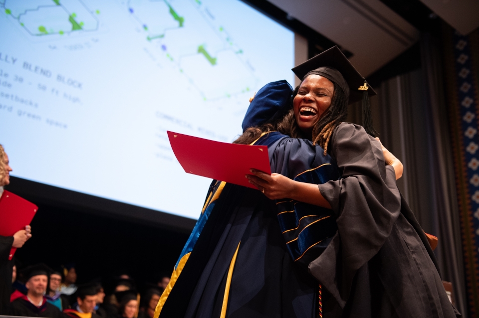 Student embraces faculty member with projection behind