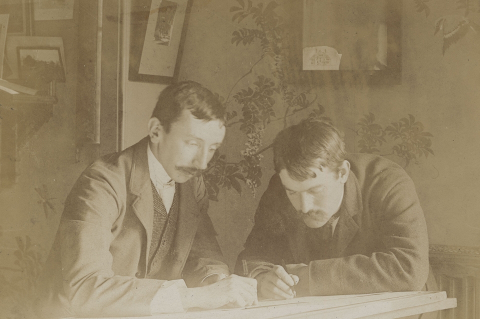 Sepia colored potrait of two male architects looking at architectural drawing