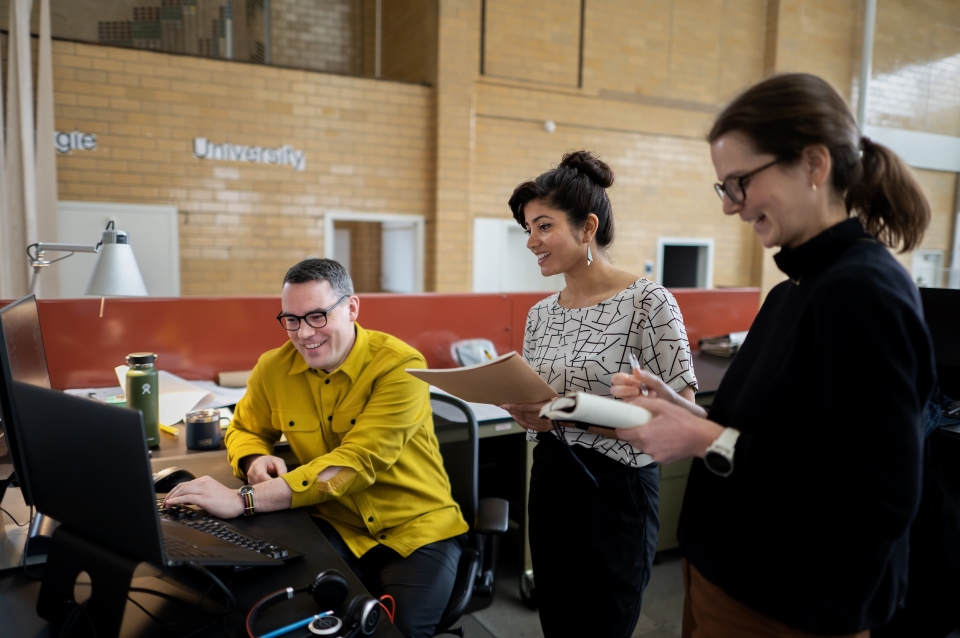A person seated at a computer shows the screen to two other people