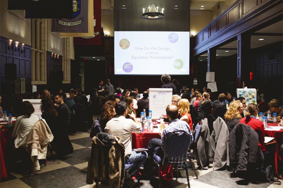 Workshop in progress. Audience seated at tables with projection in background