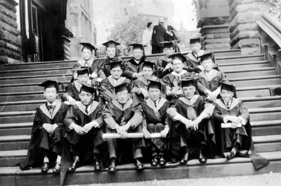 Young Chinese men in graduation robes on steps outside building