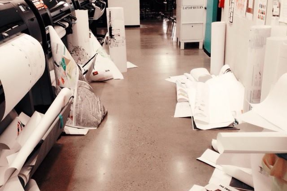 Cluttered student work space with large printers and paper on the floor