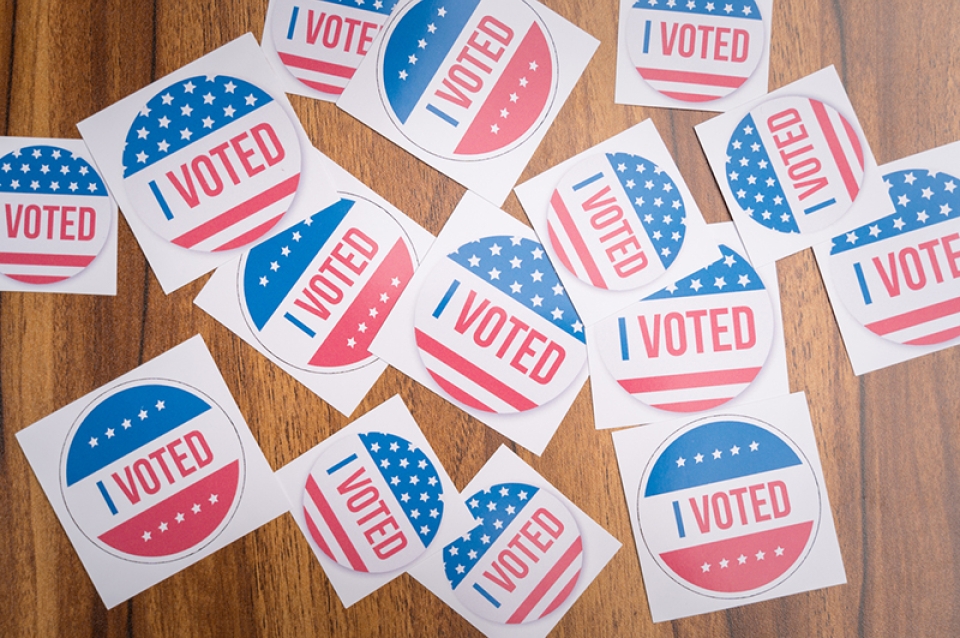Round red, white, and blue "I VOTED" stickers on a wooden table