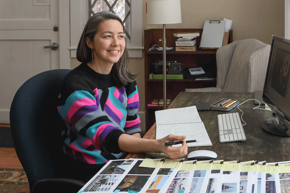 jane mah hutton is seated at a desk 