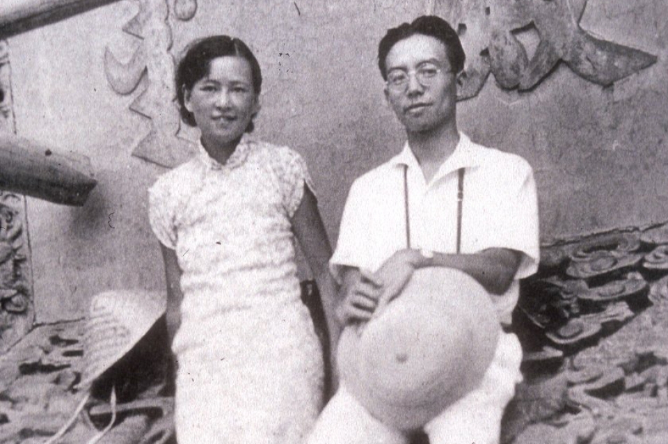 Two young Asian people standing on a tile roof pose for photo