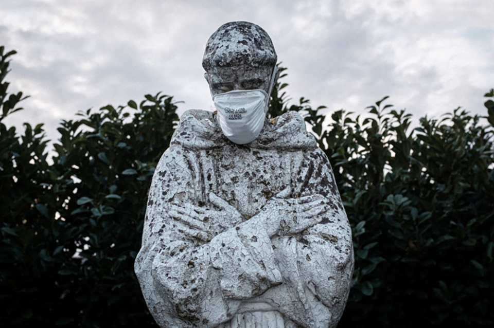 Stone statue of monk with arms folded over chest with face mask on it