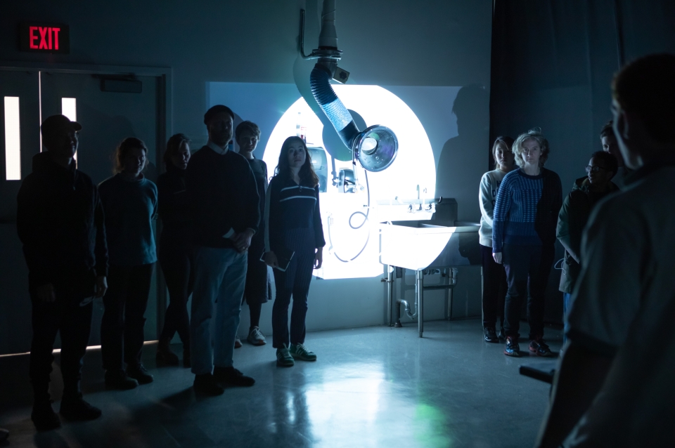 Group of students stand in darkened classroom with spotlit area