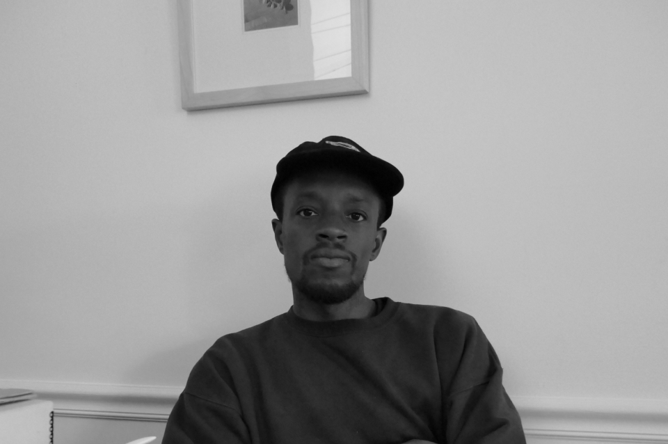 Black and white photo portrait of Yusuf Hassan sitting at a white table with papers