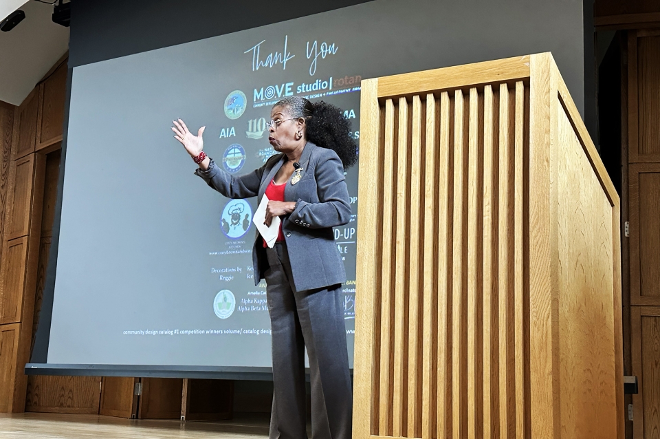 A woman on stage next to a podium gestures at audience