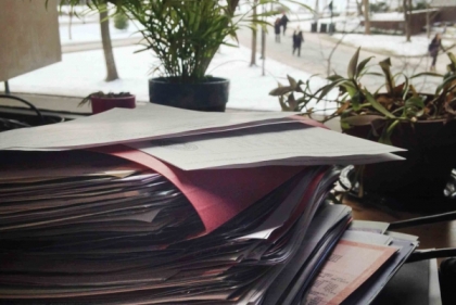 Stack of overstuffed files in an office with snow covered campus outside the window.