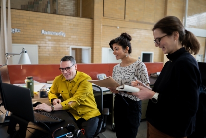 A person seated at a computer shows the screen to two other people