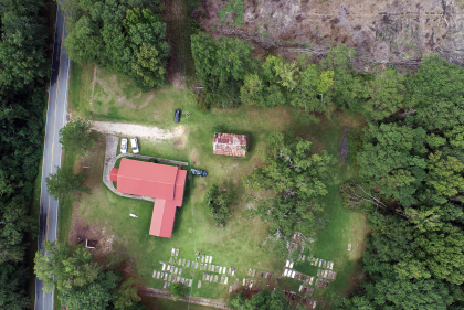 Birdseye view of grassy site with red-roofed L-shaped structure