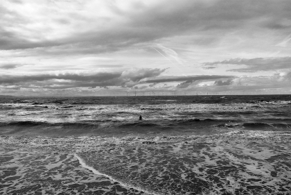 Black and white photo of an ocean coast with a sculpture of a man in the waves