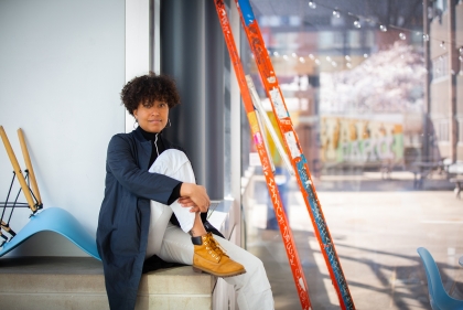 Carolyn Lazard seated on a ledge next to a ladder