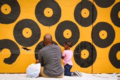 An African American man and young girl seated in front of a black and gold mural