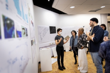 Young person in front of group gestures at posters on wall behind