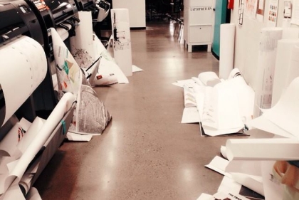 Cluttered student work space with large printers and paper on the floor