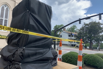 A black tarp covers a pedestal surrounded by CAUTION tape