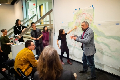 A studio instructor addresses students and critics in front of a landscape rendering