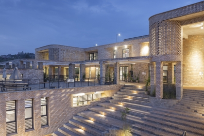  A low-slung light brick building with steps and terrace in the foreground at dusk