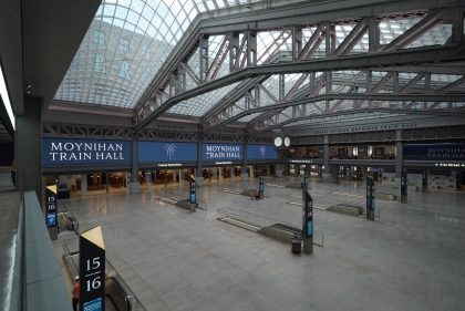 An empty stone floor punctuated by down-escalators with soaring trusses and glass roof