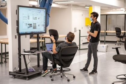 Two men, one seated, one standing looking at a large computer screen