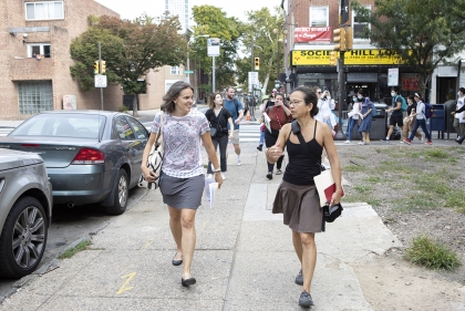 Two women walking down a sidewalk talking with a class of students following