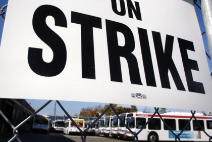 Sign on chainlink fence saying "ON STRIKE" with lot full of SEPTA buses in background
