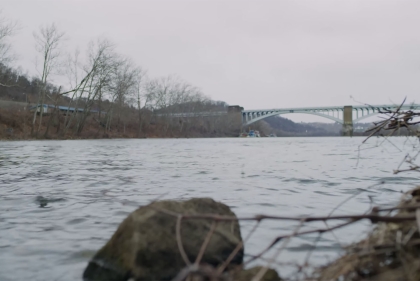 Shoreline view of urban river with bridge in the distance and boulders in the foreground