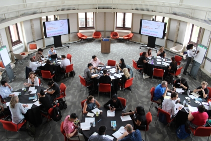 Bird's eye view of people seated at six round tables in discussion