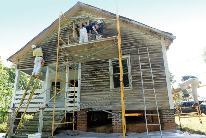 White wooden sided two story home with workers on scaffolding in front