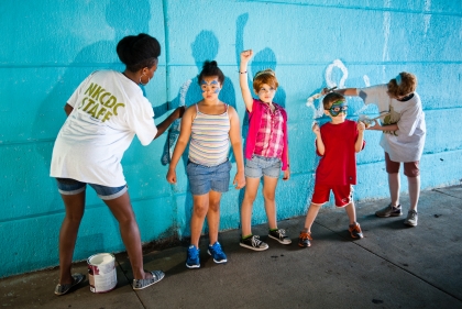 Team members Nyasha Felder and Emily Silber contribute to the interactive mural with community children