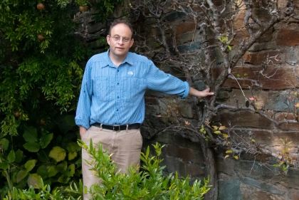 Portrait of Aaron in blue shirt standing next to a tree