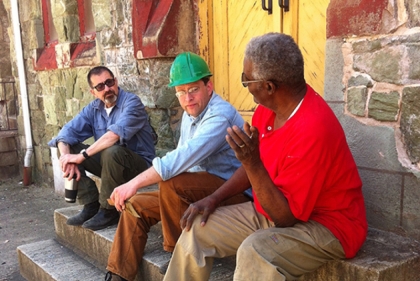 Three men seated in front of historic stone building