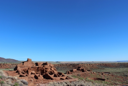 A cluster of red earthen structures under expanse of blue sky in the desert 