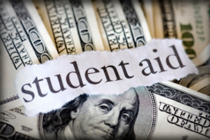 Printed words "Student aid" torn from newspaper with hundred dollar bills in the background.