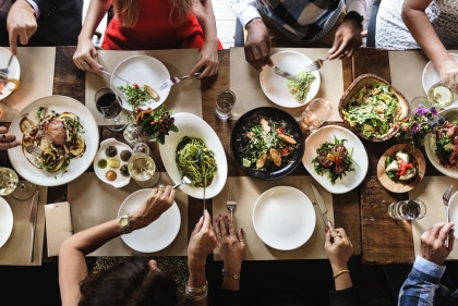 Overhead image of a table set with food and diners hands and arms cutting food and and eating.