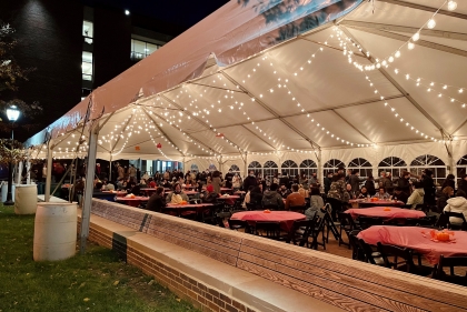 Lit up outdoor tent filled with tables and chairs all decorated for a Thanksgiving feast.