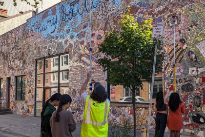 Young people hold cameras on metal rods in front of building mural